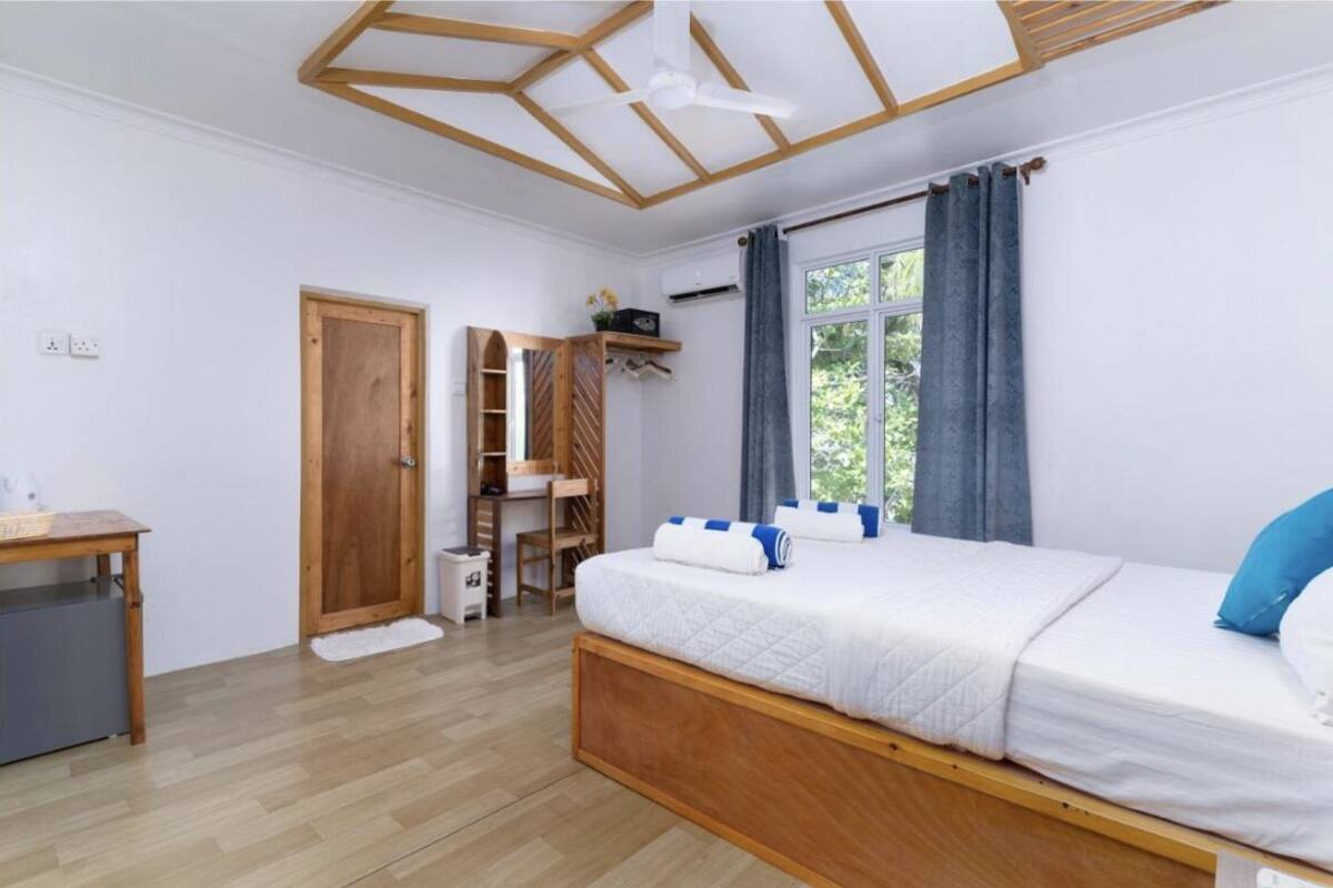 A bedroom with a wooden bed, a desk, a chair, a wardrobe, and a window with curtains.