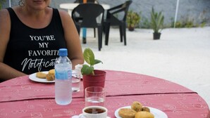 Una mesa con mantel rojo, un plato de comida, una taza de café, una botella de agua y una pequeña planta en maceta.