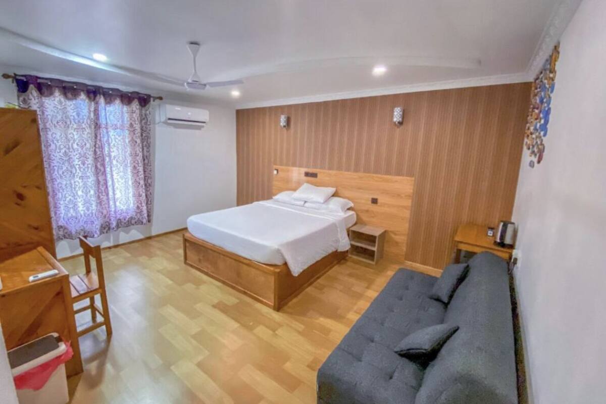 A bedroom with a wooden bed, a grey sofa, a wooden desk, and a chair.