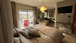 A hotel room with a large bed, a bathroom with a bathtub, a TV mounted on the wall, and a sliding glass door leading to an outdoor area. - LARGE ATYPICAL VILLA WITH PRIVATE POOL IN A QUIET LOCATION (La Farlède)
