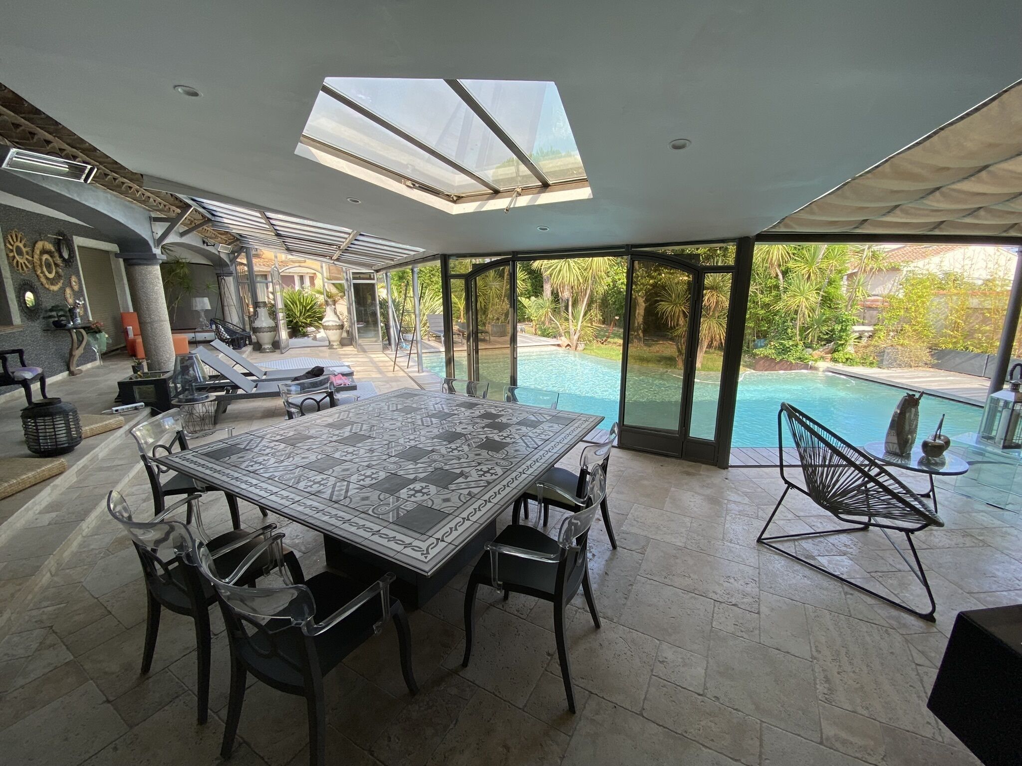 A spacious patio with a large table and chairs, a glass-enclosed swimming pool, and a view of the outdoors.