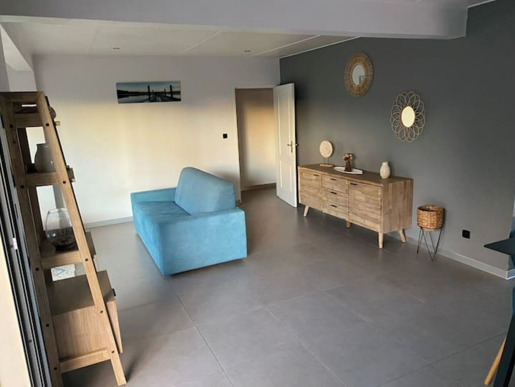 Un salon spacieux avec un canapé bleu clair, un meuble en bois et un tableau accroché au mur.