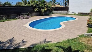 A swimming pool with a wooden deck, surrounded by greenery and a white building. - Villa with swimming pool in the center of st louis river (Saint-Louis)