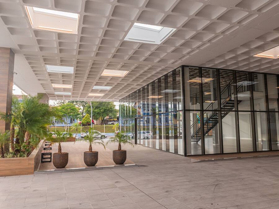 Entrada moderna de edifício com fachada de vidro, escadaria e plantas em vasos.