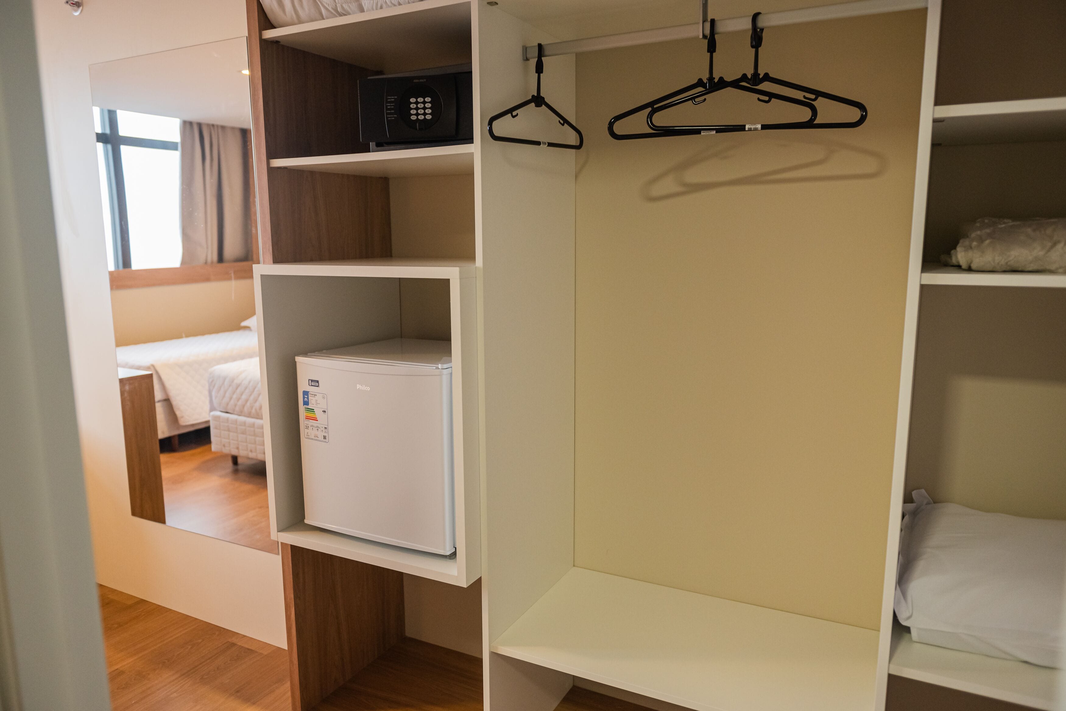 A hotel room with a bed, a mini-fridge, a radio, and a wardrobe with hangers.