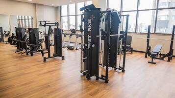 A gym with various exercise machines, large windows, and a wooden floor.