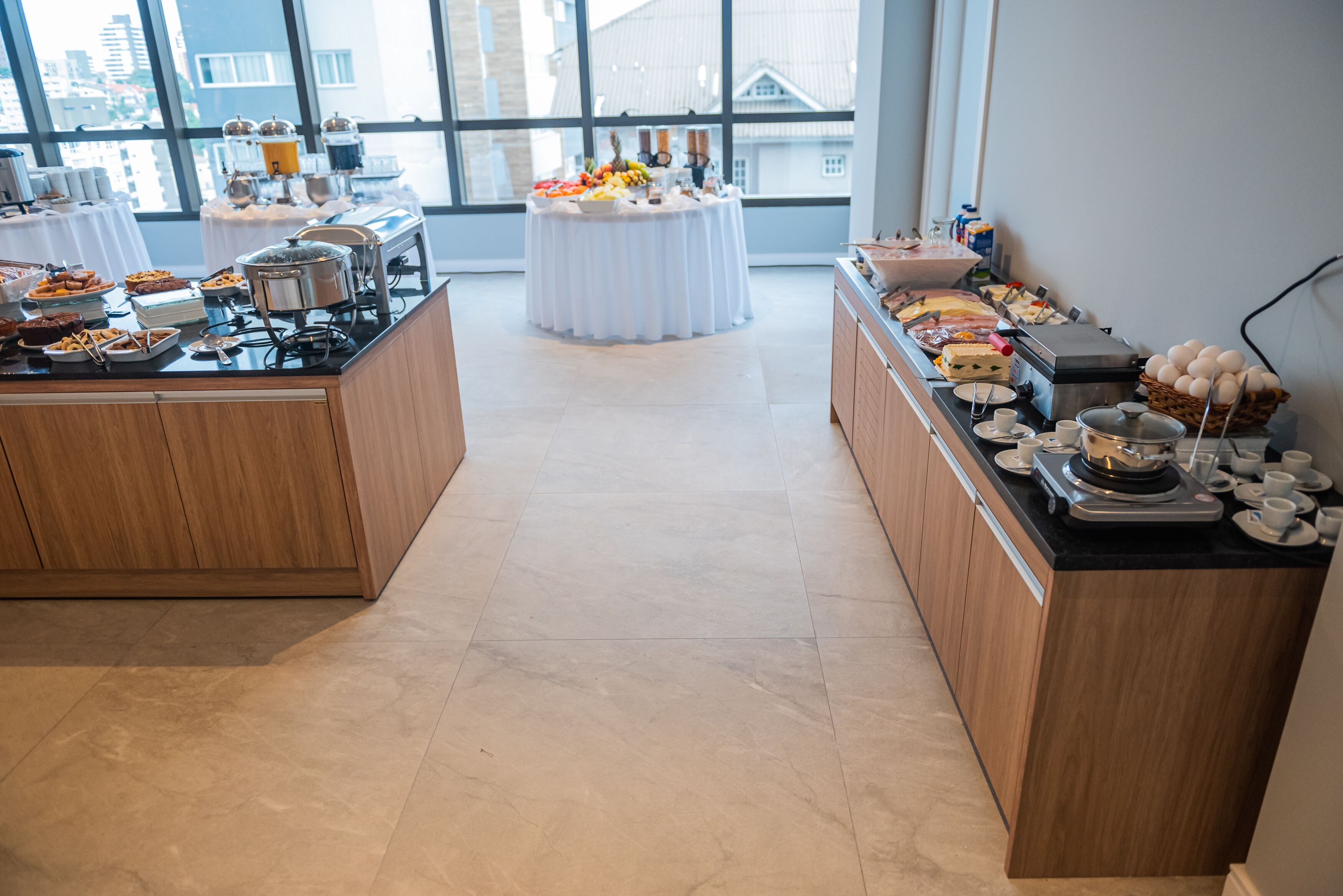A buffet setup with various food items and a coffee station in a bright room with large windows.