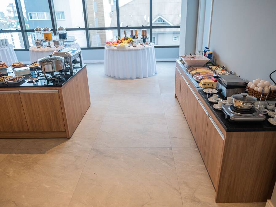 A buffet setup with various food items and a coffee station in a bright room with large windows.