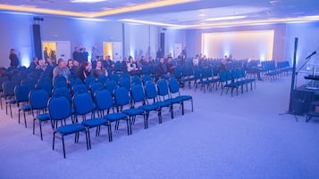 Una sala de conferències amb files de cadires blaves, un escenari amb un púlpit i una pantalla gran.