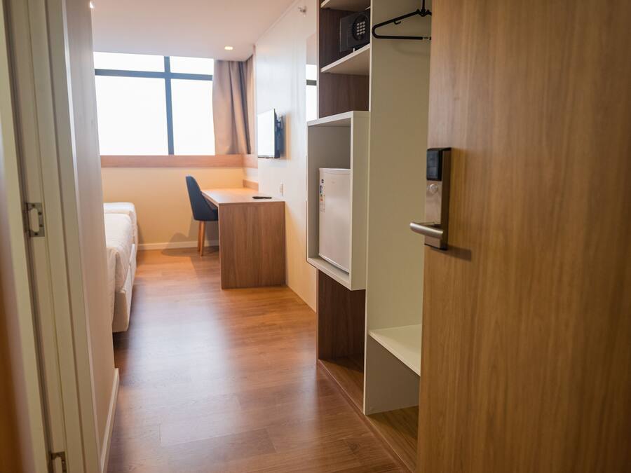 A hotel room with a wooden floor, a bed, a desk, a chair, and a wardrobe.
