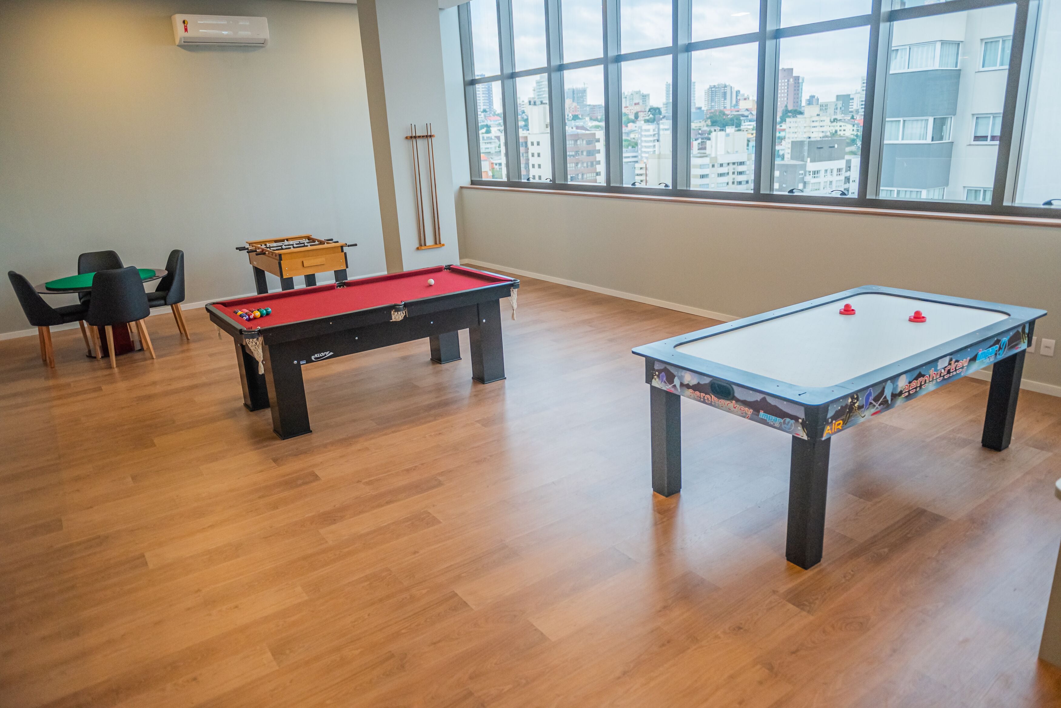 Quarto com duas mesas de pebolim, mesa de bilhar e janela com vista para a cidade.