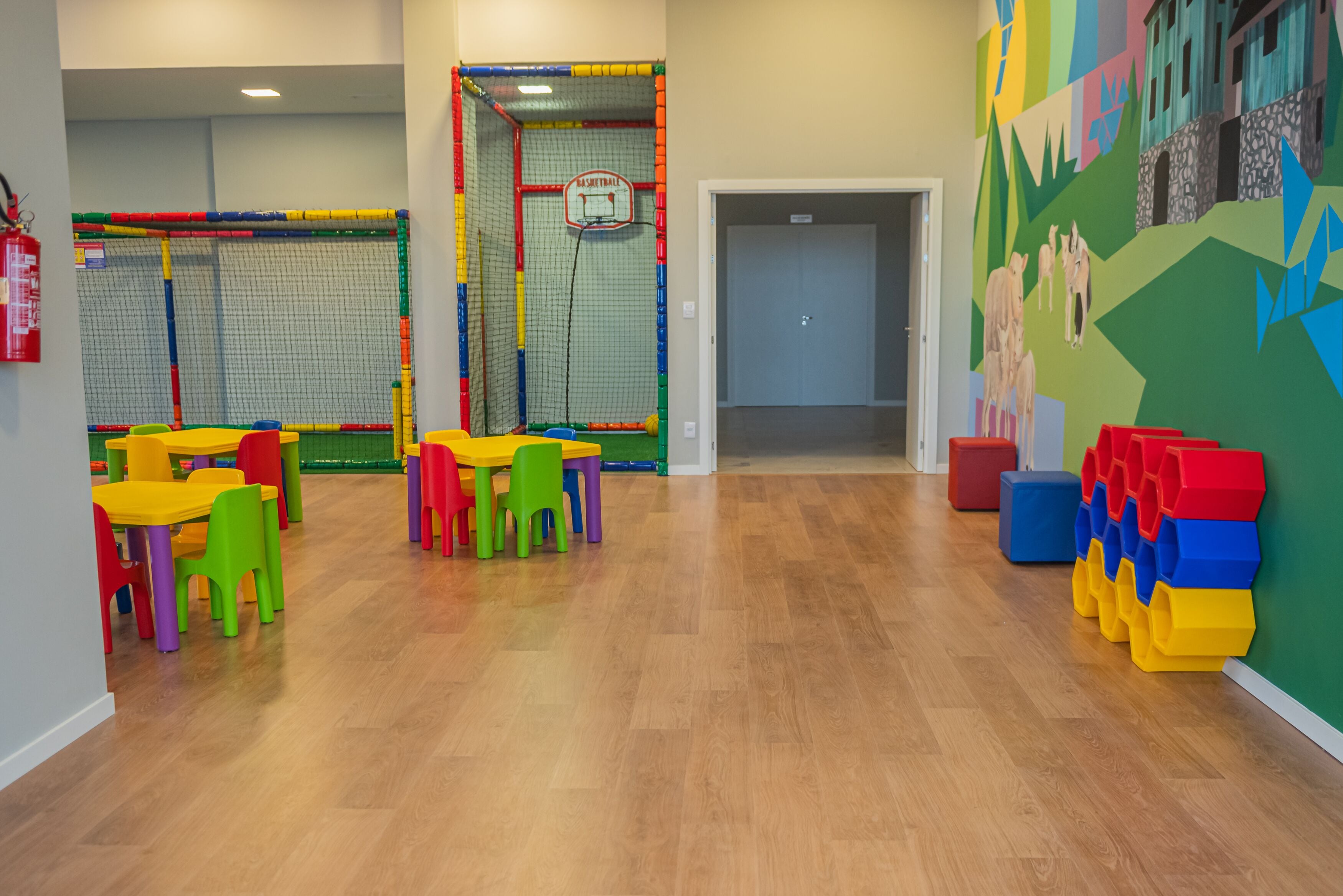 Ein hell erleuchteter Indoor-Spielbereich mit bunten Spielgeräten und einem Basketballkorb.