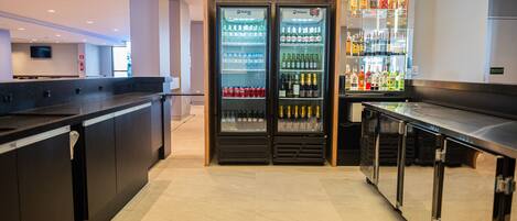 Un área de bar moderna con dos refrigeradores Imbesa llenos de bebidas, una barra con pileta y una exhibición de diferentes botellas de licor.