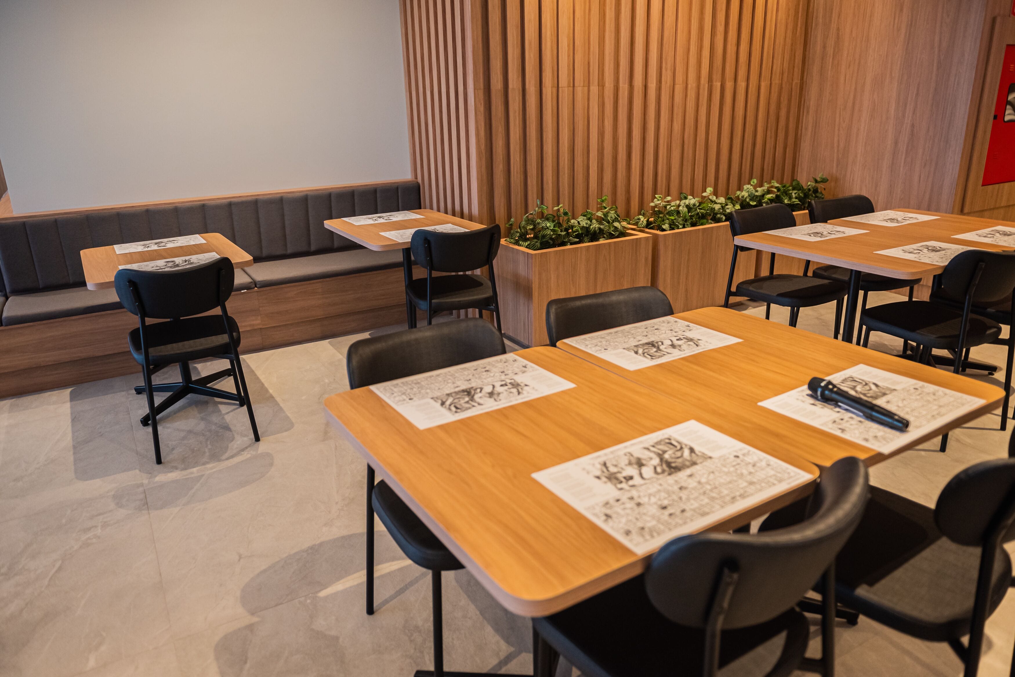 A conference room with wooden tables and black chairs, equipped with name cards and a projector screen.
