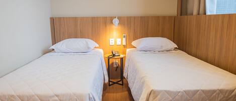 A hotel room with two single beds, a bedside table with a phone, and a wall-mounted light.