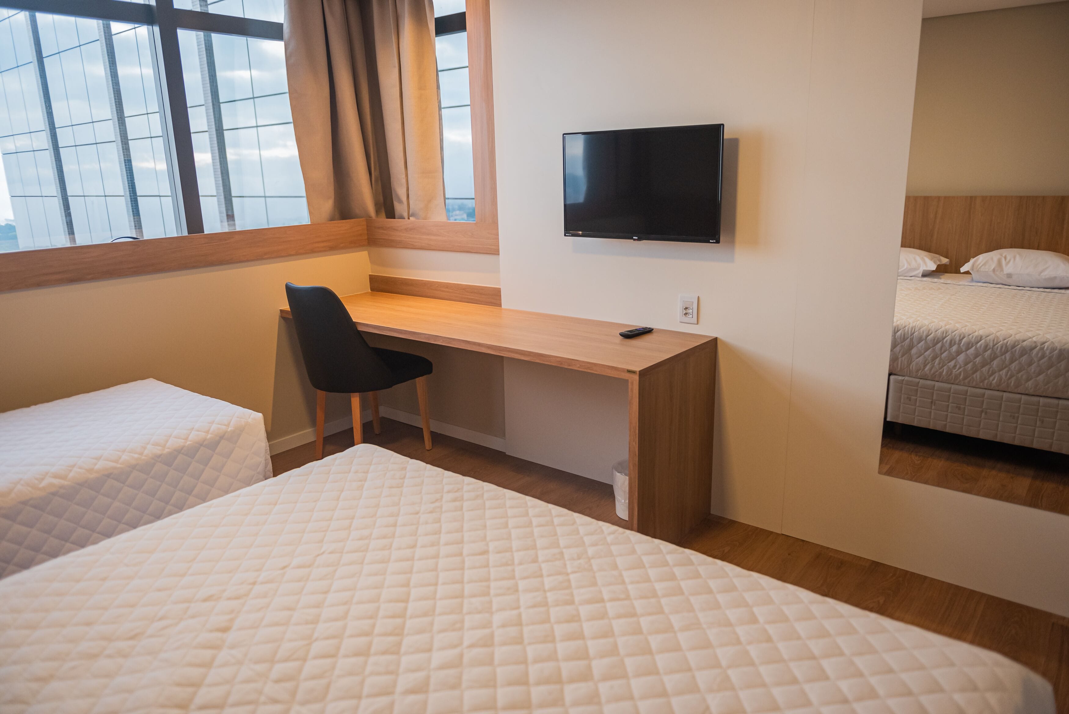 Habitació d'hotel amb dos llits, una taula amb cadira, televisió i finestra amb cortines.