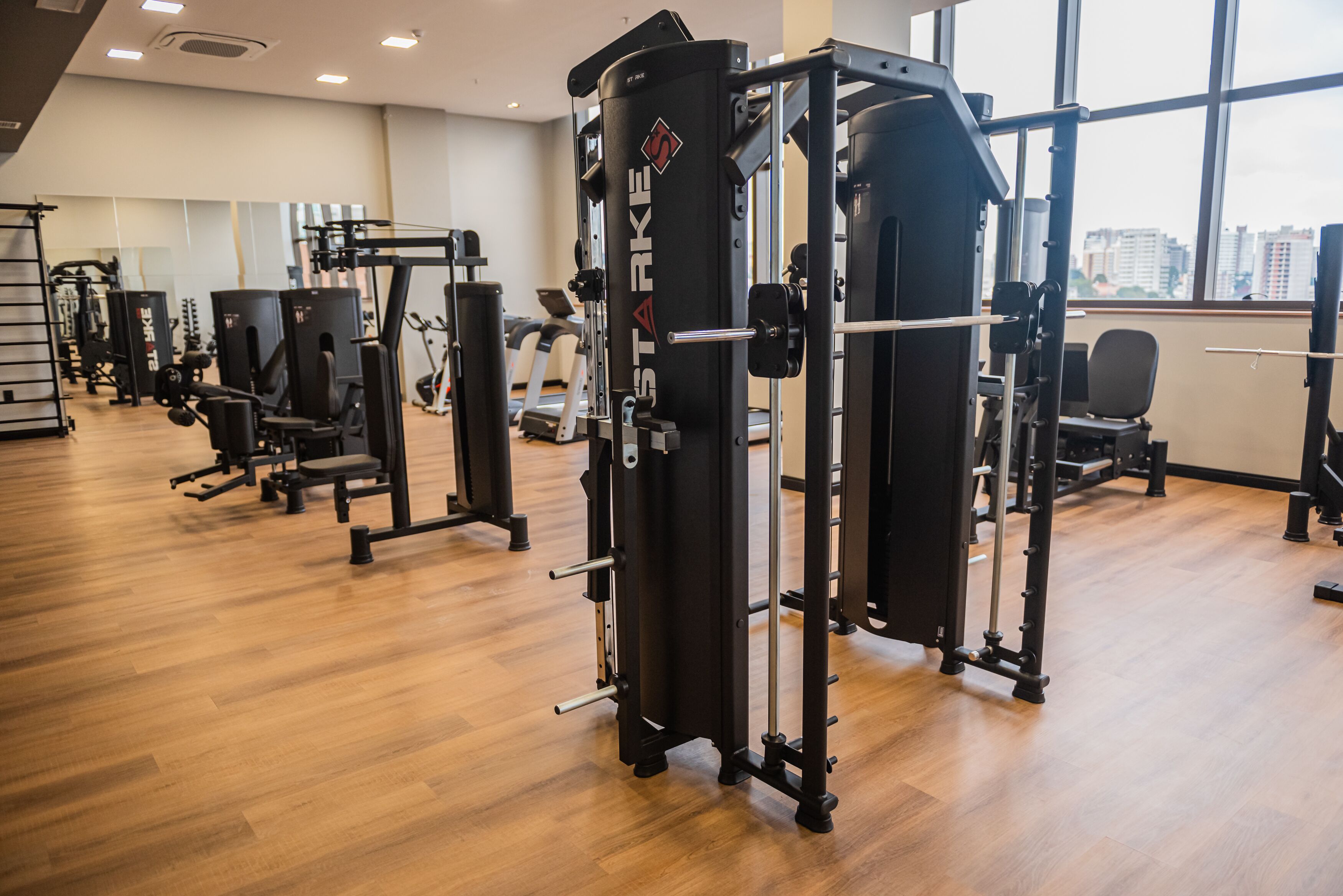 A gym with various exercise machines, a treadmill, and a window with a city view.