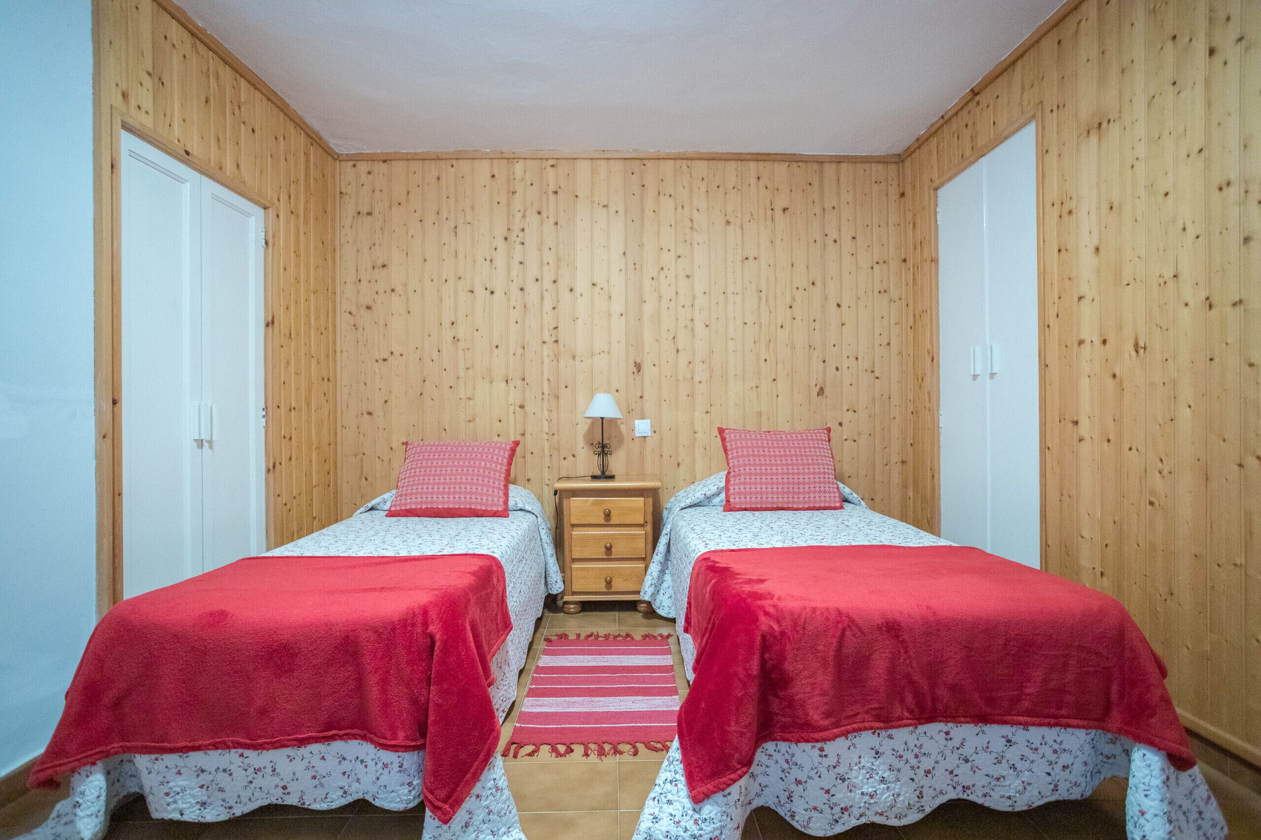 Een kamer met twee bedden, houten wanden, een klein houten nachtkastje en een rode vloerkleed.