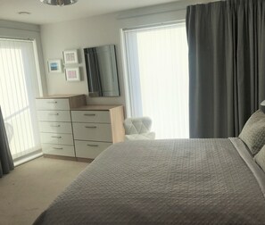 Une chambre à coucher avec un lit, une commode, une chaise et une fenêtre avec des rideaux.
