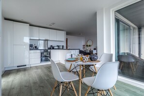 Une cuisine moderne avec des meubles blancs, un coin repas comprenant une table ronde et quatre chaises, et une grande fenêtre donnant sur l’extérieur.
