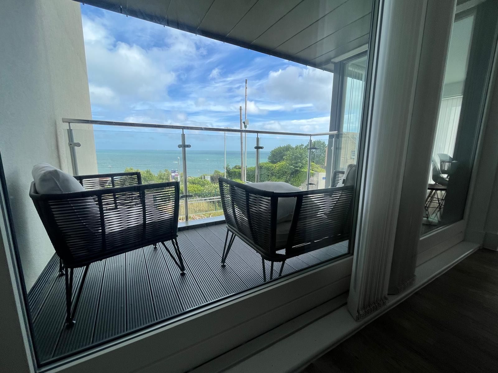 Un balcon avec deux chaises et une table, donnant sur une étendue d’eau et sur de la verdure.