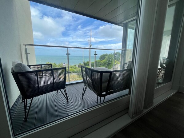 A balcony with two chairs and a table, overlooking a body of water and greenery.
