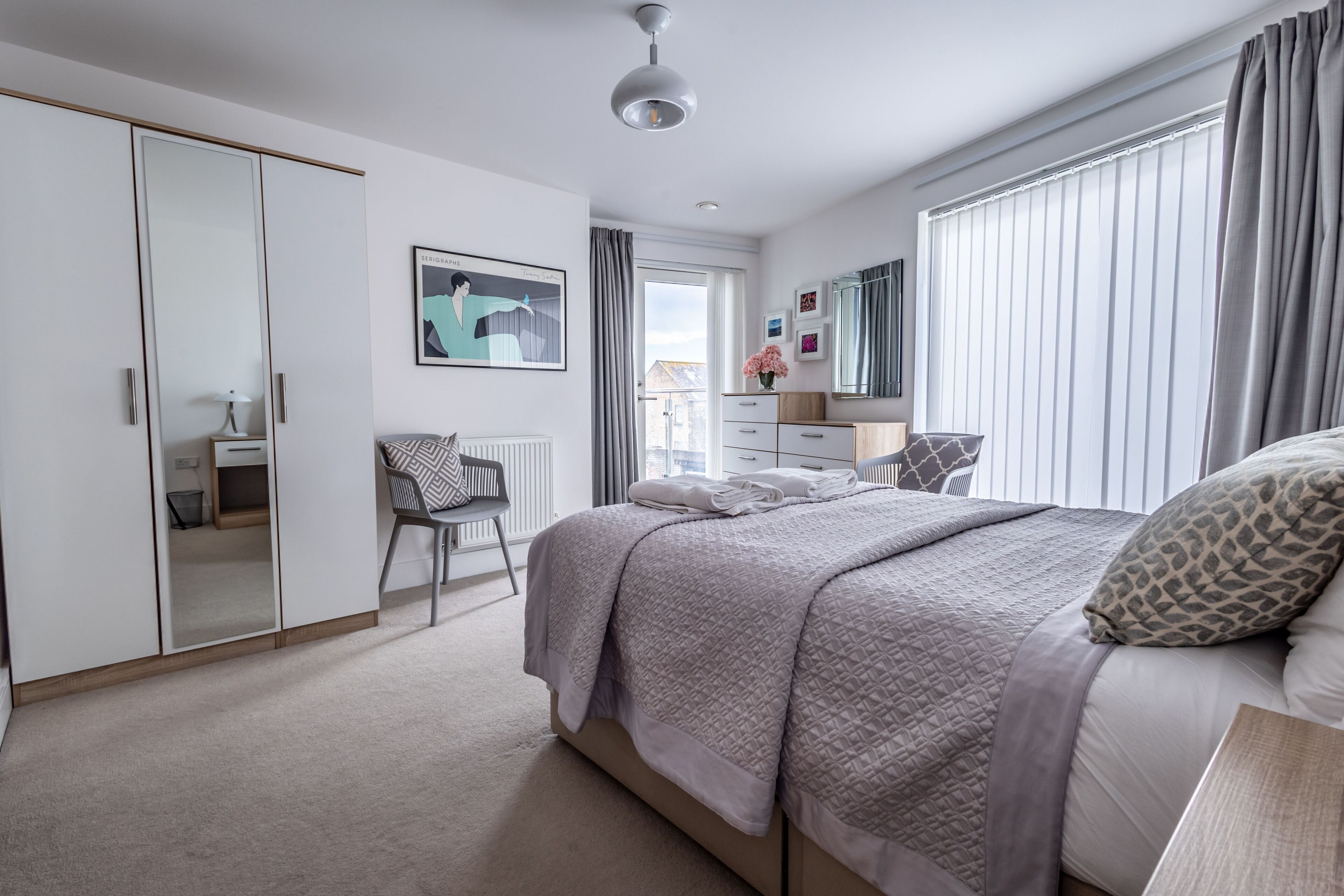 A modern bedroom with a large bed, a wardrobe, a desk, and a chair.