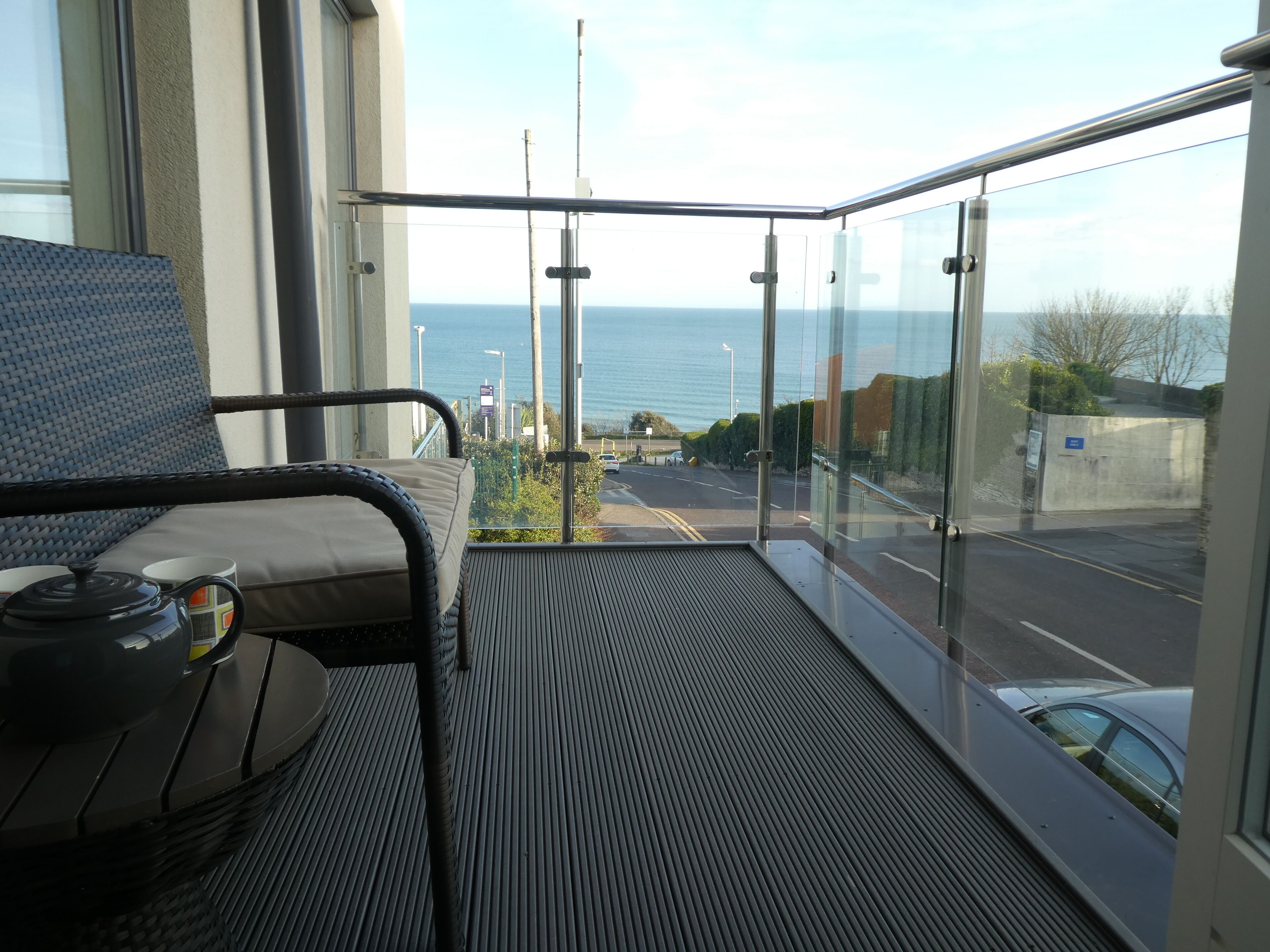 A balcony with a view of the sea, a chair, and a table with a teapot and cup.