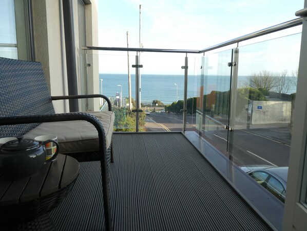 Un balcón con vista al mar, una silla y una mesa con tetera y taza.