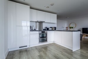 Une cuisine moderne avec des meubles blancs, des appareils en acier inoxydable et un plancher en bois.