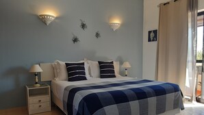 A bedroom with a bed, two bedside tables, a nightstand, a wall-mounted light fixture, and a window with curtains. - Casa Rosa Montes (Lagos)