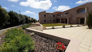 A two-story building with a tiled courtyard, surrounded by greenery and a well-maintained garden. - Casa Rosa Montes (Lagos)