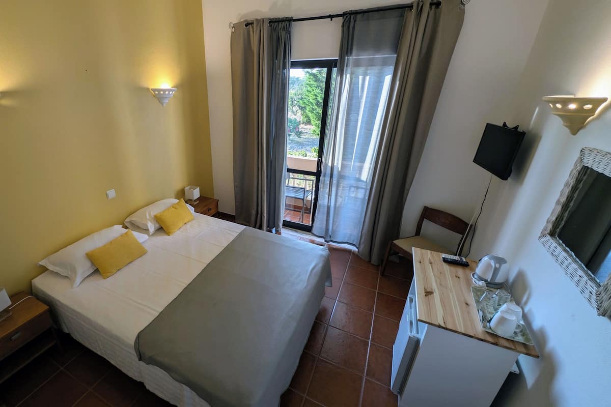 Une chambre d’hôtel comprenant un lit, des tables de chevet, un bureau avec une chaise, une télévision et un balcon avec des rideaux.