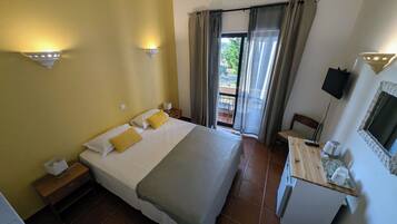 A hotel room with a bed, bedside tables, a desk with a chair, a TV, and a balcony with curtains.