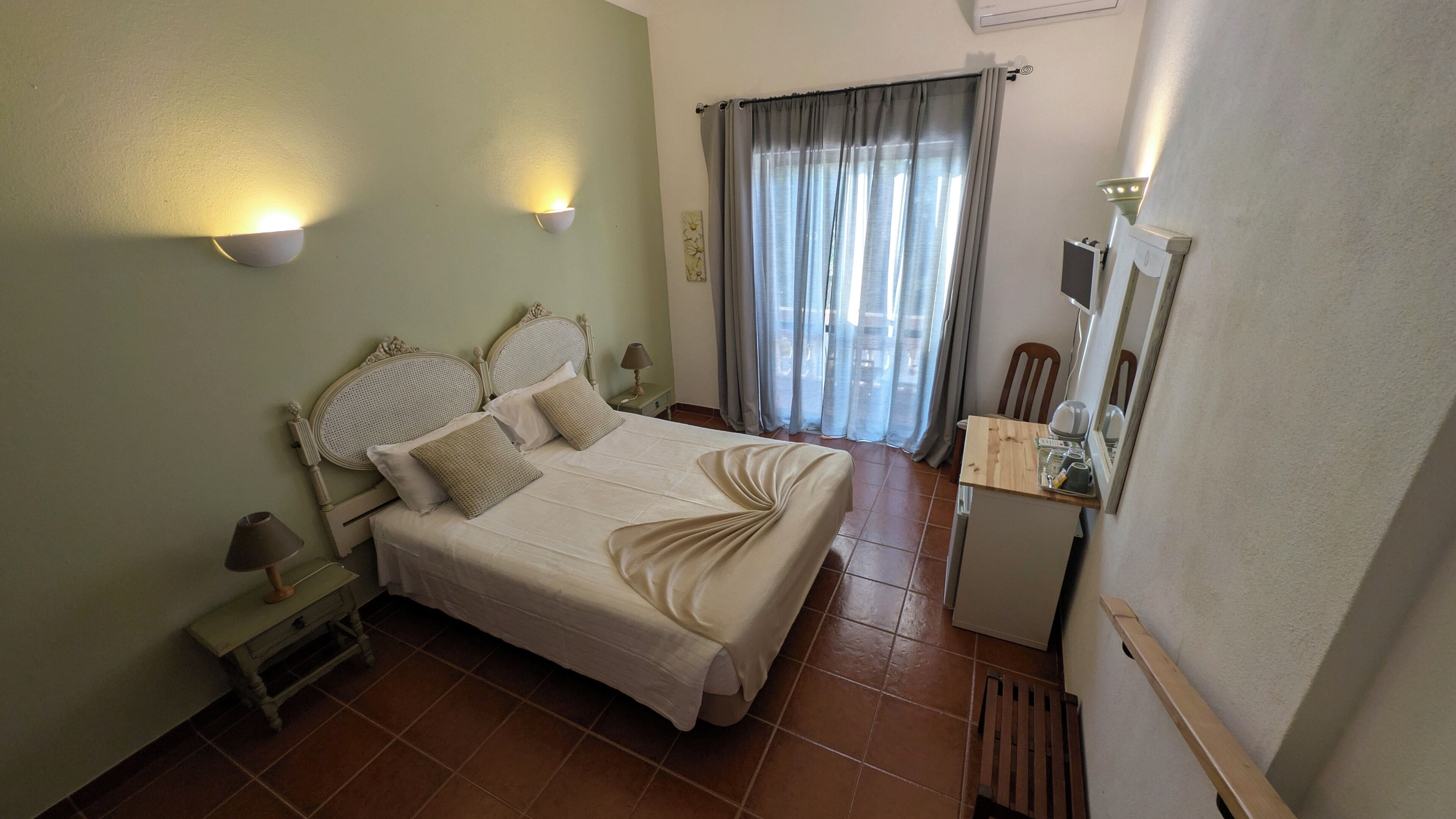 A neatly arranged bedroom with a bed, bedside tables, a desk, and a window with curtains.