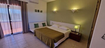 A hotel room with a bed, a nightstand, a lamp, a window with curtains, and wall-mounted lights.