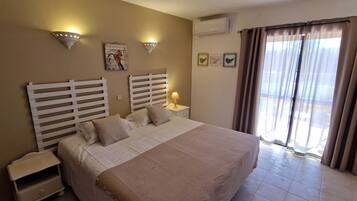 Een slaapkamer met een groot bed, twee nachtkastjes, een wandairconditioner en een raam met gordijnen.