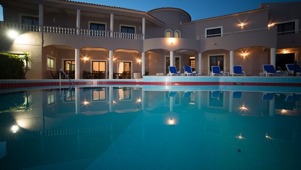A swimming pool with lounge chairs and a building with multiple balconies. - Casa Rosa Montes (Lagos)