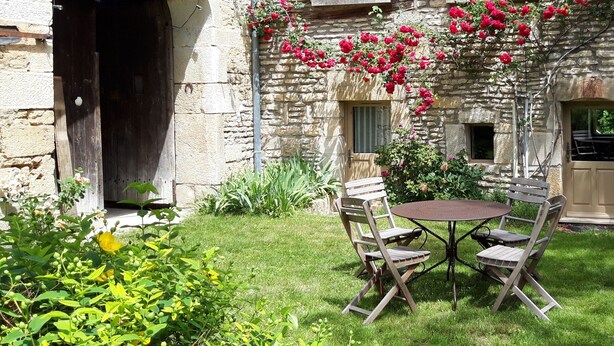 Un bâtiment en pierre avec une table ronde et quatre chaises dans le jardin.