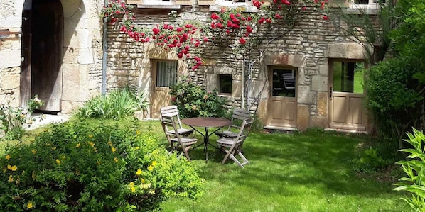 Un bâtiment en pierre doté d’un patio avec jardin, comprenant une table et des chaises.