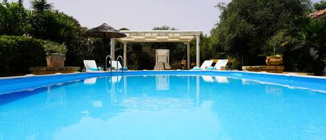 Une piscine avec des chaises longues et une pergola.