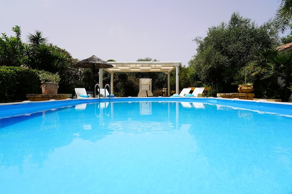 Una piscina con sillas de descanso y una pérgola.