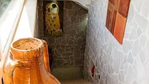 Una jarra de terracota grande en un rincón, un muro de piedra con un mural y un piso de baldosas.