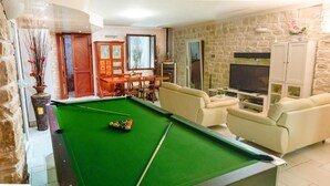 Una mesa de billar en una habitación con paredes de piedra, un televisor y un armario.