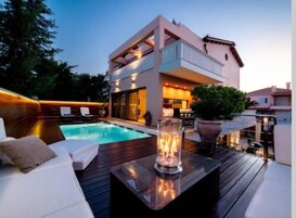 Una casa moderna de dos pisos con piscina, mobiliario exterior y un patio bien iluminado.