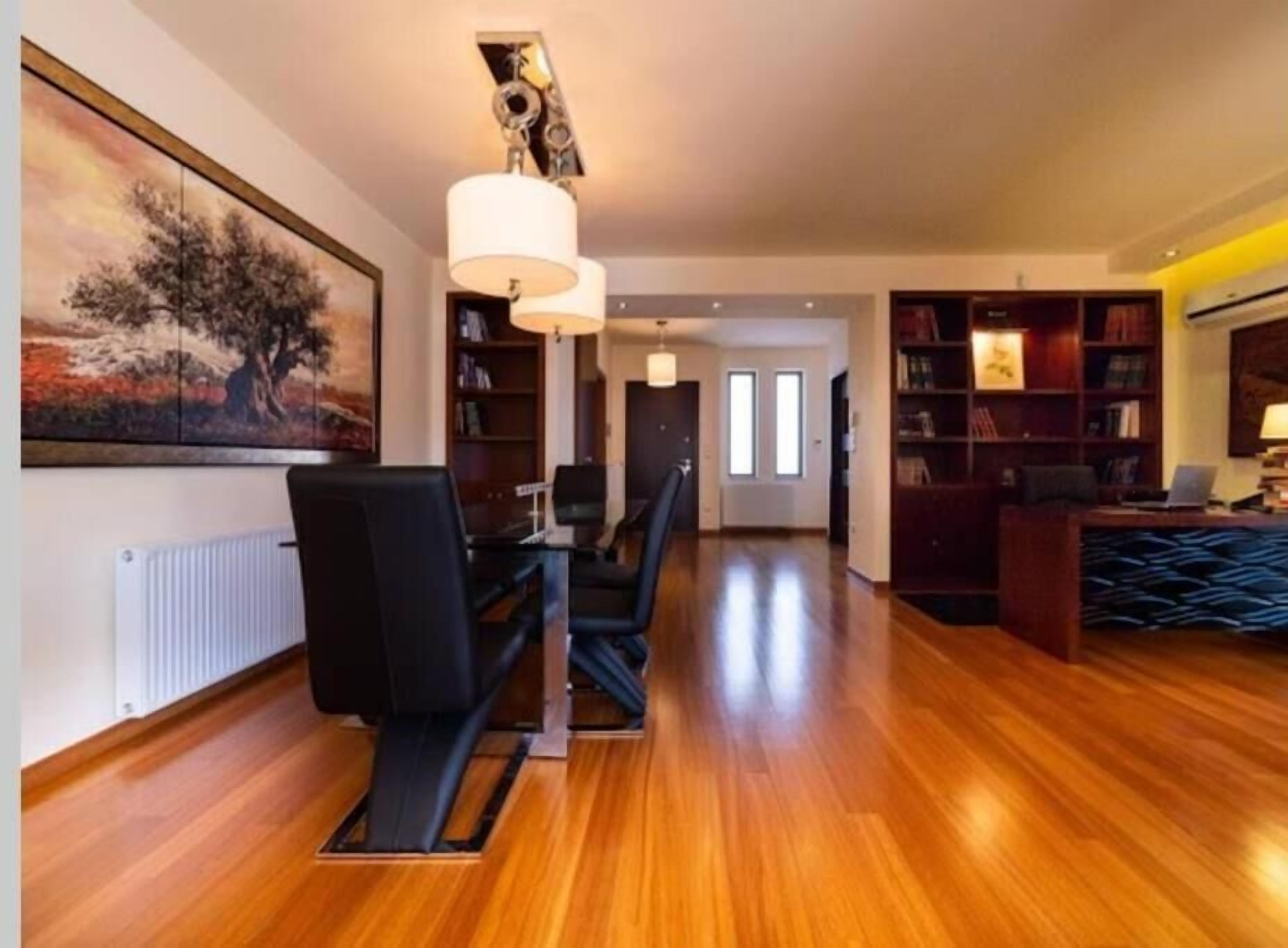 A spacious room with a wooden floor, a dining table with chairs, a bookshelf, and a painting on the wall.