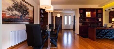 A spacious room with a wooden floor, a dining table with chairs, a bookshelf, and a painting on the wall.