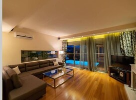 Una sala de estar moderna con un sofá, una mesa de centro, un televisor de pantalla plana y vista a una piscina.