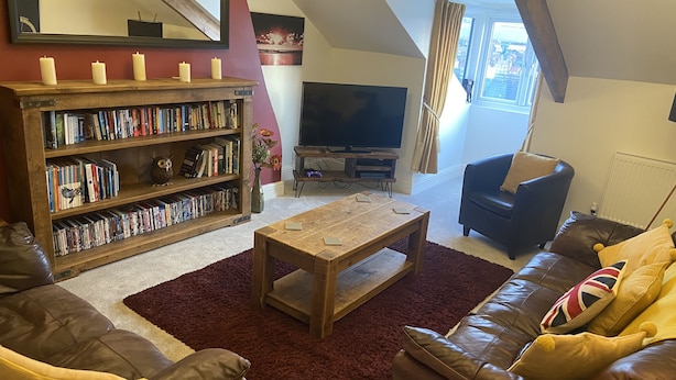 A cozy living room with a fireplace, bookshelves, a television, and leather sofas. - Stunning Whitby Penthouse Apartment with Abbey View (Whitby)