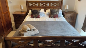 A wooden bed with a cross-back design, flanked by nightstands with lamps, and a wall-mounted painting above. - Stunning Whitby Penthouse Apartment with Abbey View (Whitby)